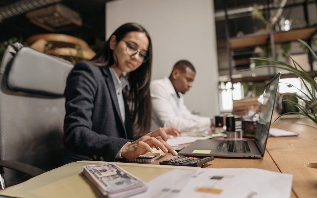 A businesswoman uses a calculator and laptop next to cash, showcasing how outsourced accounting can help your business grow faster.